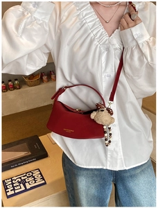Detail of dark red leather crescent bag with bear charm worn with white ruffle shirt
