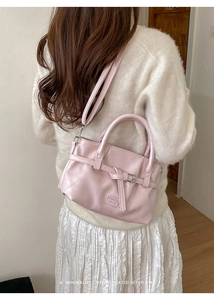 Detail of pink crossbody bucket bag with decorative buckle and metal brand plate