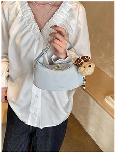 Close-up of light blue crescent bag with a cute plush bear charm and golden logo
