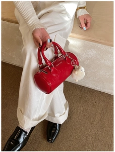 Detail of red cylindrical Boston bag with plush sheep charm and silver logo text