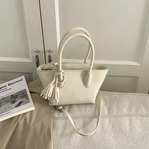 Détail d'un sac seau beige minimaliste avec pampille et bandoulière réglable