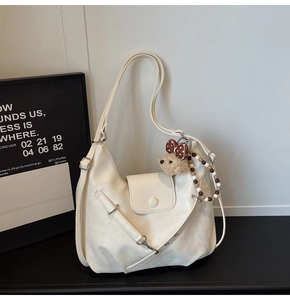 Detail of a creamy white tote bag with a cute bear charm and beaded tassel decoration