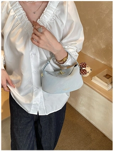 Close-up of light blue leather handbag with golden lock and cute bear charm on a model