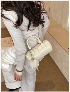 Detail of creamy white cylinder bag with shiny leather finish and plush charm