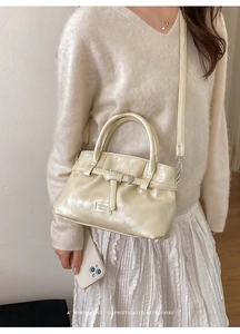 Detail of a creamy white glossy leather bucket bag with silver buckle and detachable strap