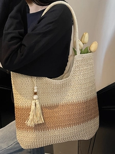 Large woven straw tote bag with beige and brown stripes and a decorative tassel pendant