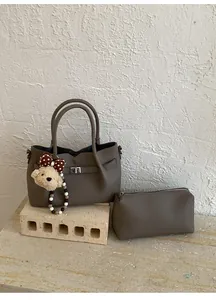 Détail d'un sac à main gris texture litchi avec pochette assortie et charm ours
