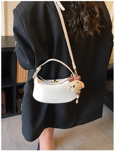 Detail view of white half-moon leather shoulder bag with cute brown bear charm on model