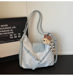 Detail of light blue semi-moon shoulder bag with soft faux leather texture and bear charm