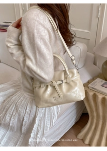 Close-up of cream leather handbag with decorative buckle and adjustable shoulder strap