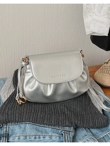 Détail du sac bandoulière argenté avec base plissée et logo tendance sur le rabat