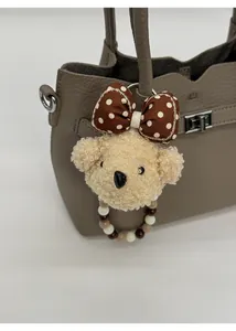 Détail d'un charme d'ours en peluche avec nœud à pois et anneau perlé sur un sac en cuir