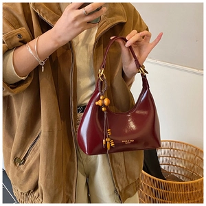 Detail of burgundy hobo bag with patent leather finish and unique wooden bead charm