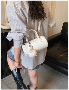 Close-up of a white leather barrel bag with a plush charm and gold hardware detail