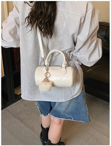 Detail of a creamy white barrel bag with a plush lamb charm and adjustable shoulder strap