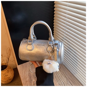 Detail view of silver cylindrical bag with metallic leather texture and plush charm