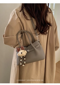 Détail du sac seau taupe en cuir grainé avec fermoir rotatif sur un trench-coat kaki