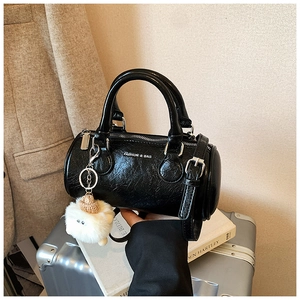 Detail of black cylindrical barrel bag with pleated leather texture and white plush charm