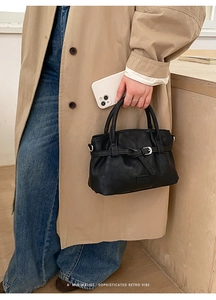 Close-up of a minimalist black leather handbag with wrap-around belt detail on a model
