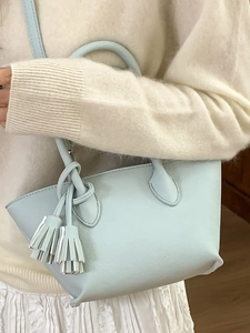 Sac seau bleu clair minimaliste à pompons porté avec un pull et une jupe plissée blanche