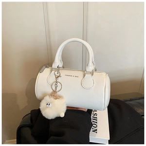 Close-up of white cylinder handbag featuring a plush charm and silver zipper detail