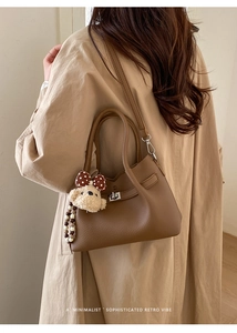 Détail du sac seau marron avec motif litchi et breloque chien en peluche sur trench
