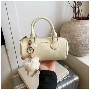 Close-up of cream cylinder handbag with pebble texture and cute plush monster charm