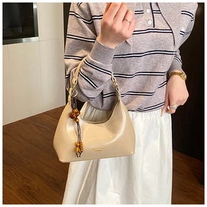 Detalle de bolso hobo beige con texto clásico y borla vintage de cuentas de madera