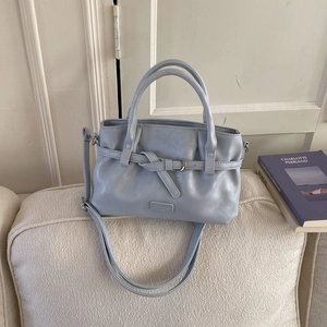 Close-up of a light blue-grey leather bucket bag with decorative buckle on a woven sofa