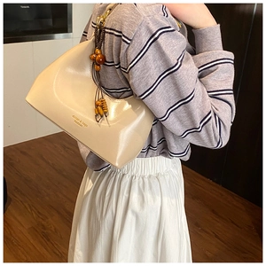 Detalle del bolso de hombro beige curvo con dije de madera y texto del logotipo