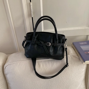 Close-up of black pleated faux leather handbag with buckle strap and long shoulder strap