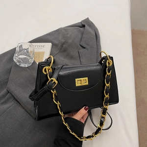 Close-up of black glossy leather handbag featuring golden metal turn-lock and chain strap