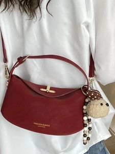 Deep red half-moon shoulder bag with gold metal lock and plush ball charm accessory