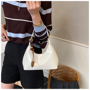 Detalle de bolso de hombro blanco con texto dorado y accesorio de cuentas de madera
