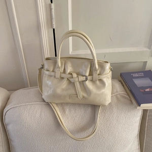 Detail of a creamy white pleated leather handbag with metallic logo on a textured sofa