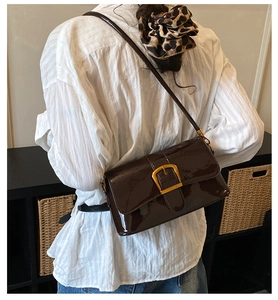 Detail of glossy chocolate brown patent leather shoulder bag with golden buckle closure