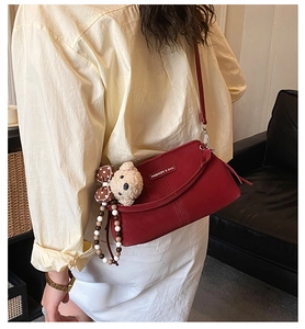 Detail of burgundy crossbody bag with bear charm and beaded strap on leather surface