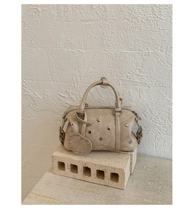 Détail du sac Boston beige avec rivets étoilés et breloque cœur sur support brique