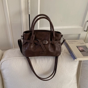 Detailed view of deep brown vintage bucket bag with buckle and logo on white sofa