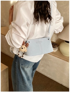 Detail of light blue crossbody bag with plush bear charm and stylish bow on model