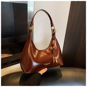 Detalle de un bolso hobo marrón brillante con flecos de madera y anillas de metal dorado