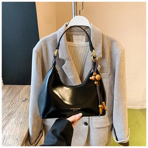 Detalle de bolso hobo negro brillante con borla de cuentas de madera y asa trenzada