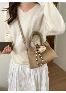 Détail du sac seau en cuir grainé kaki avec breloque ours sur jupe blanche