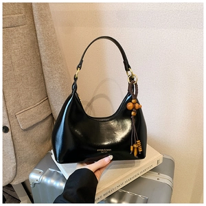 Detalle del bolso Hobo negro de media luna con acabado brillante y colgante de borla de cuentas