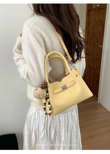 Détail du sac seau jaune clair avec texture grainée, fermoir en métal et breloque