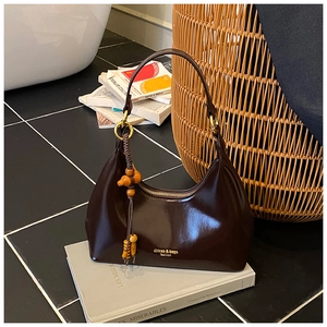 Detalle de un bolso hobo marrón oscuro brillante con aros dorados y colgante de cuentas