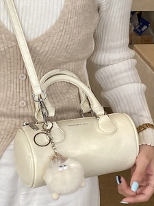 Chic beige cylinder barrel handbag with plush monster charm and leather shoulder strap