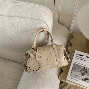 Détail du sac Boston beige avec rivets étoiles en métal et charm cœur sur un canapé