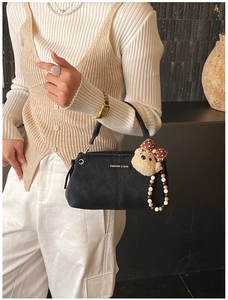 Detail of black matte shoulder bag with plush bear charm and fashion metal logo