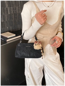 Close-up of black suede crossbody bag featuring fashion metal logo and teddy bear charm